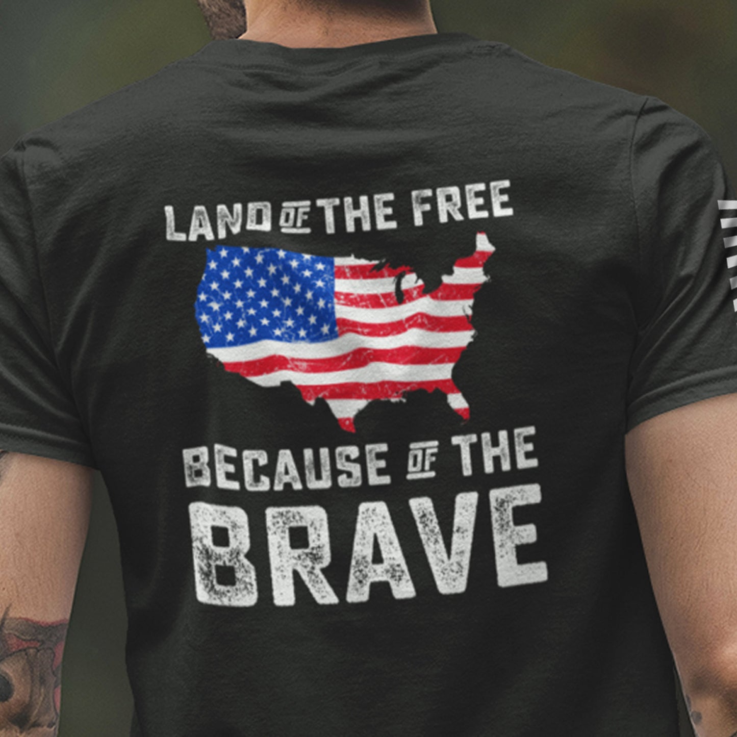 Close up of the back of man wearing Land of the Free Because of the Brave t-shirt with distressed USA map in American flag design and bold white patriotic text.
