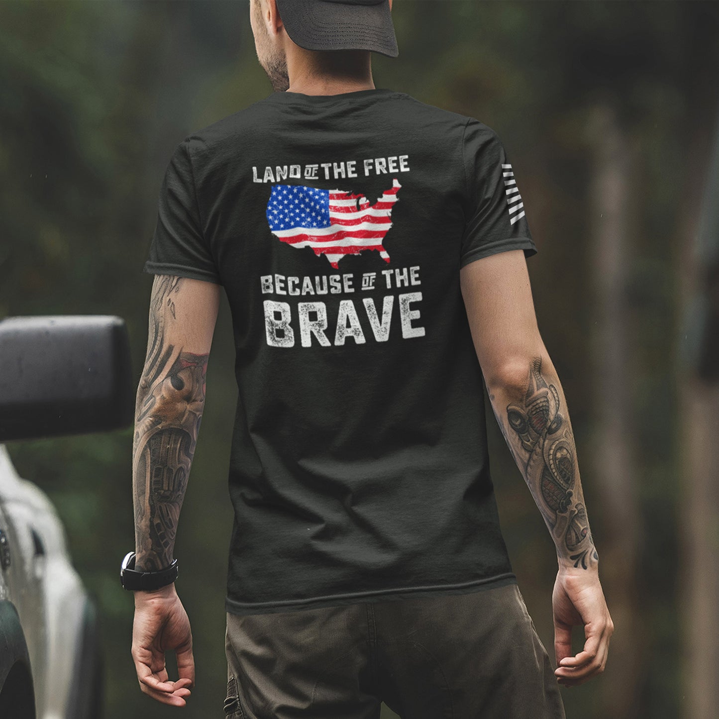 Back of man wearing Land of the Free Because of the Brave t-shirt with distressed USA map in American flag design and bold white patriotic text.