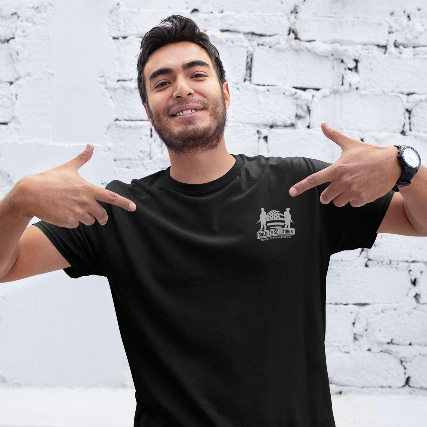 Man wearing Soldier Solutions patriotic t-shirt with front logo and sleeve American flag print, styled in a casual pose against a neutral background.