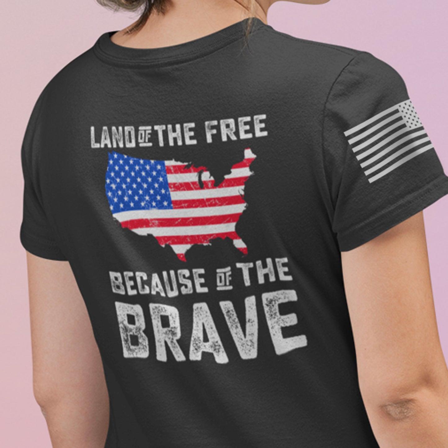 Close up of a back view of woman wearing Land of the Free Because of the Brave t-shirt with U.S. map graphic in American flag colors and distressed bold text.