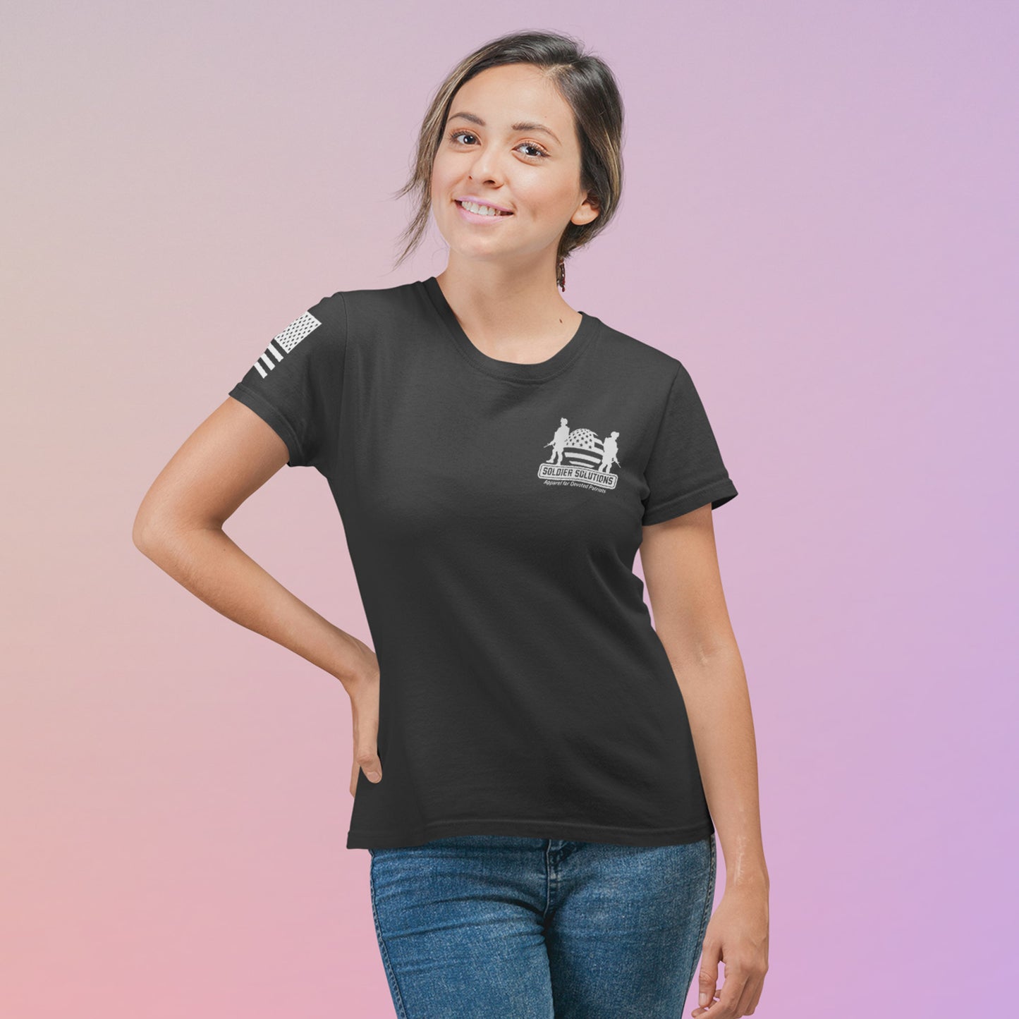 Woman wearing black Soldier Solutions t-shirt, front chest logo and sleeve American flag visible, standing in front of a soft gradient background.