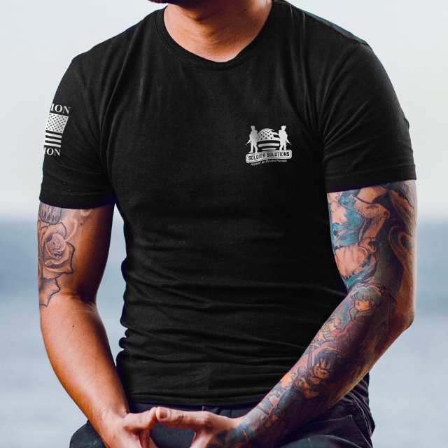 Man seated wearing Stand for Something shirt featuring Soldier Solutions front logo and sleeve design