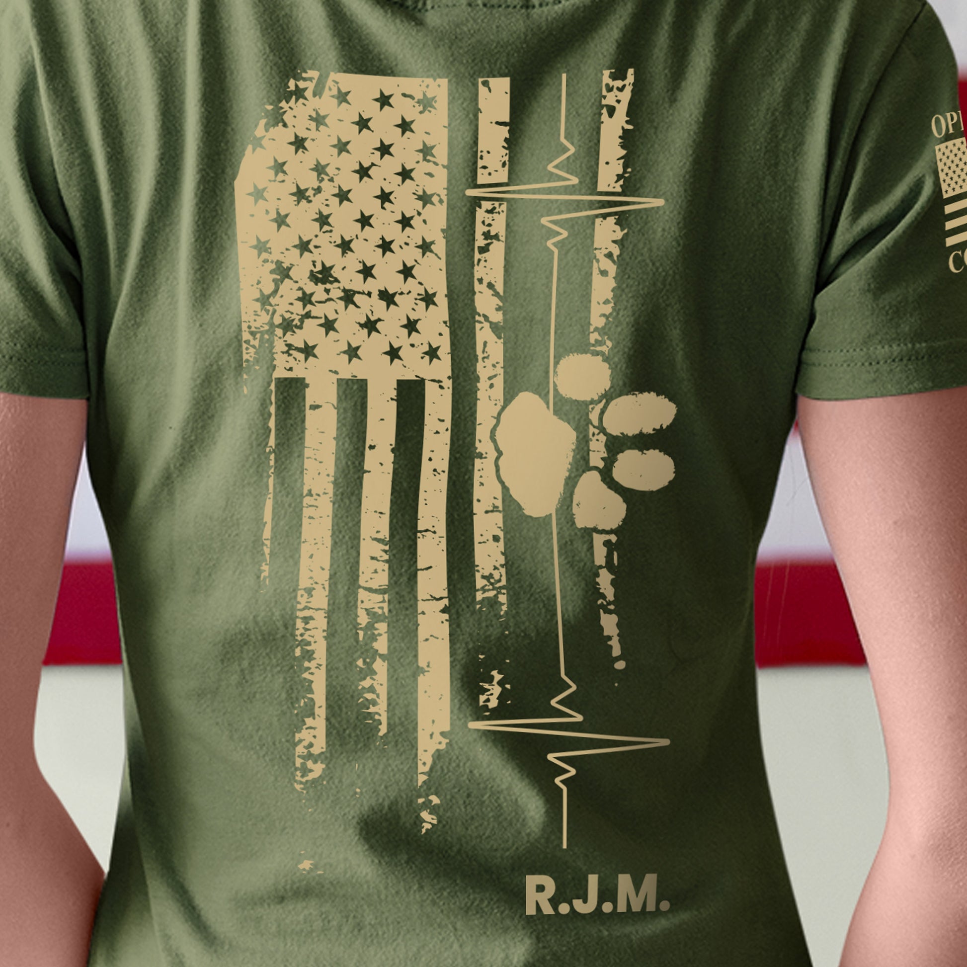 Back of memorial t-shirt featuring distressed American flag, heartbeat line, paw print, and tribute initials honoring a veteran lost to suicide.
