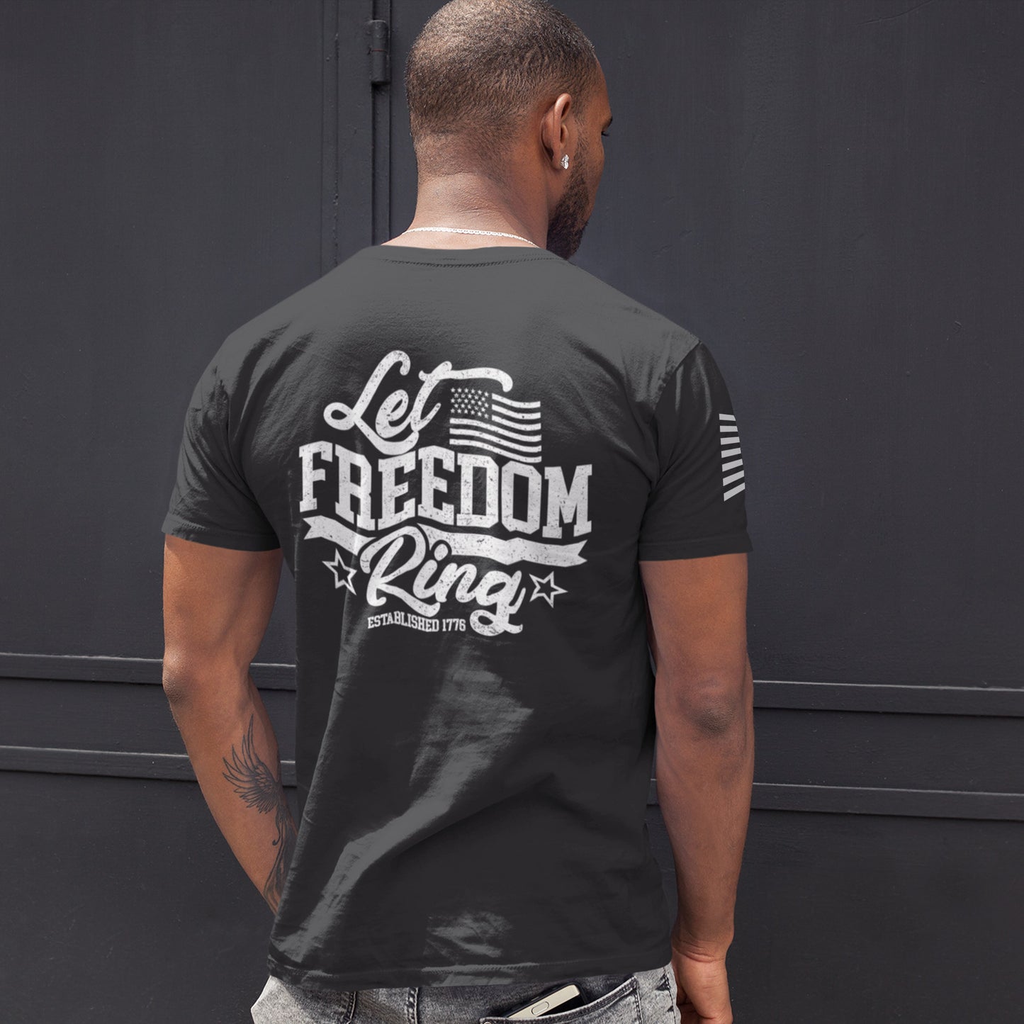 Back of man wearing Let Freedom Ring t-shirt with bold distressed text ‘Let Freedom Ring – Established 1776’ and patriotic star details.
