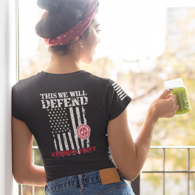 Woman wearing black patriotic shirt with distressed American flag and "This We Will Defend" print