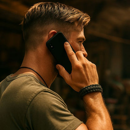 Man wearing black paracord survival bracelet with tactical design while on phone call.
