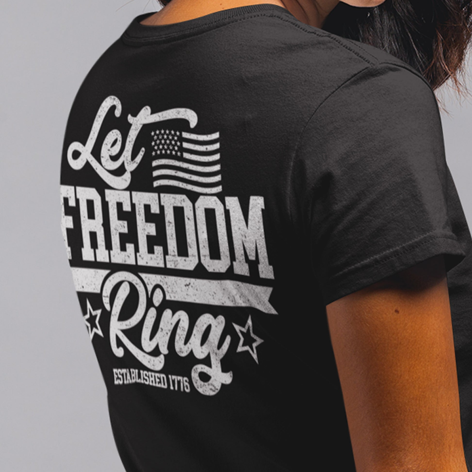 Close up back view of woman in Let Freedom Ring patriotic shirt showing bold ‘Let Freedom Ring – Established 1776’ text and American flag sleeve design.”