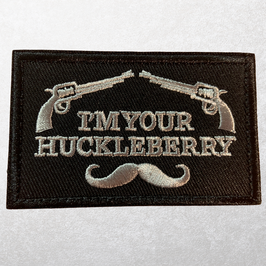 Hook-and-loop tactical patch with “I’m Your Huckleberry” text, crossed revolvers, and mustache embroidery.