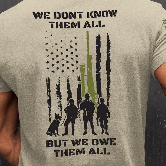 Close-up of men’s tribute t-shirt with distressed flag, soldier and K9 silhouettes, and We Don’t Know Them All message.